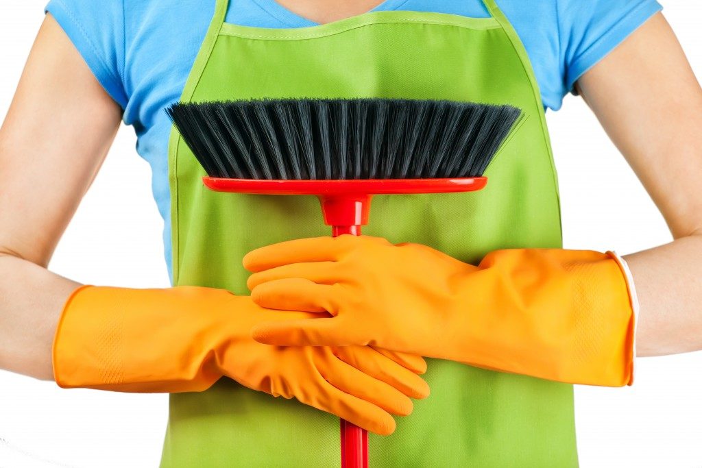 Woman wearing apron and cleaning gloves while holding a broom