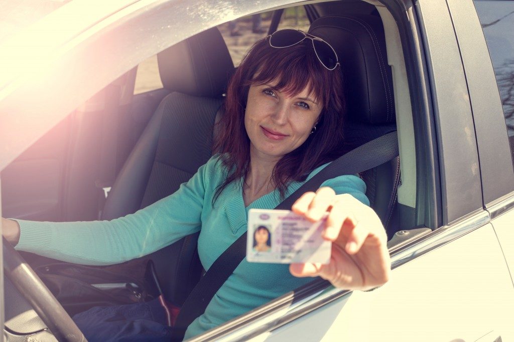 Woman holding out her driver's license while inside the car